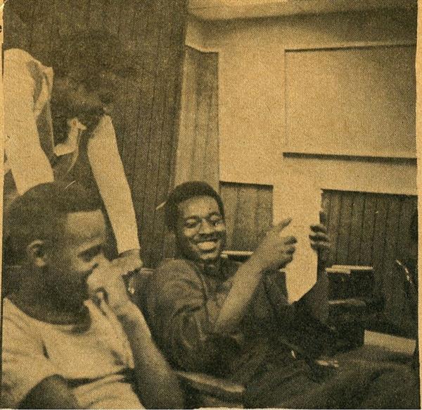 Three men review a script and laugh seated in a theater